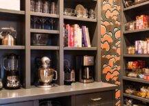 Pantry features black cabinets and custom shelves with orange and black wallpaper.