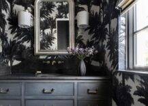 Black and white powder room with black and white Pierre Frey Mauritius wallpaper features a silver leaf French mirror over a black washstand with a black marble curved backsplash.