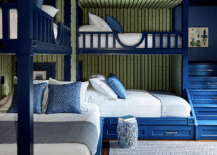 Bedroom features blue L-shaped built in bunk beds with blue built in staircase, green striped wallpaper and a blue rug.