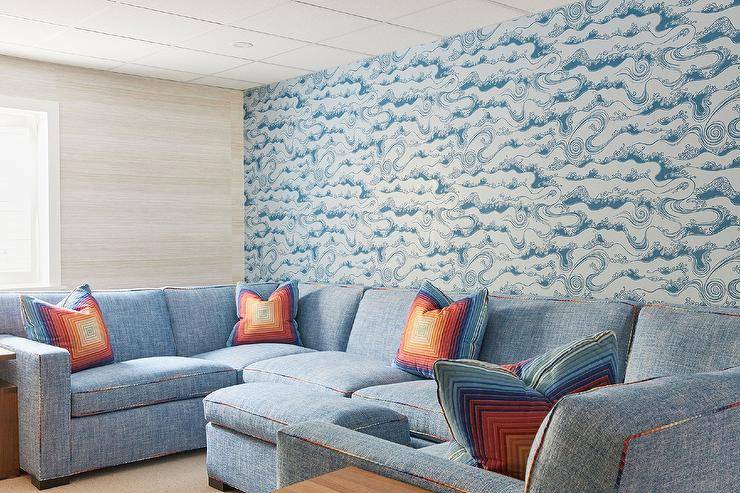Living room features a blue U-shaped sectional with rainbow piping accented with orange and blue concentric pillows and blue waves wallpaper.