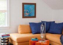 Modern attic orange and blue family room with beadboard trim features an orange sectional with blue pillows, orange lacquer cluster accent tables, atop blue carpet.