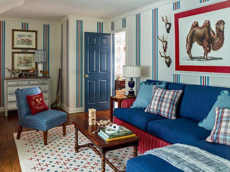 Living room features a red and blue skirted sofa with vintage spindle coffee table atop a red and blue rug, a blue accent chair and a blue door.