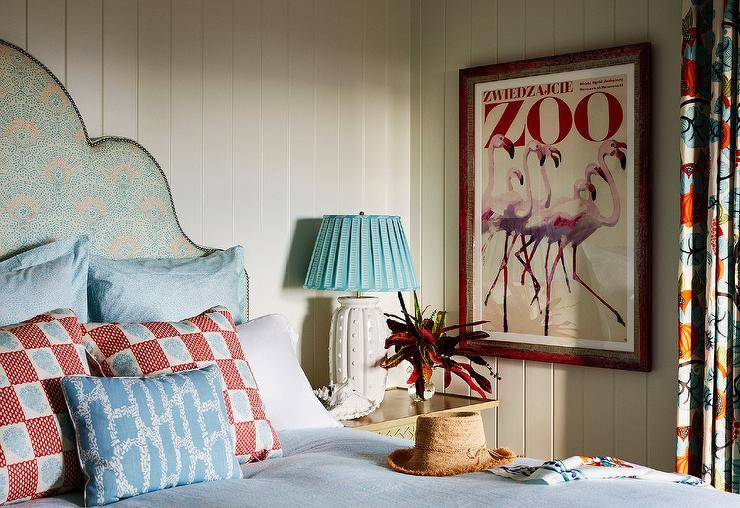 Bedroom features an orange and blue headboard with red and blue bedding lit by a sky blue pleated lamp on a white lamp.