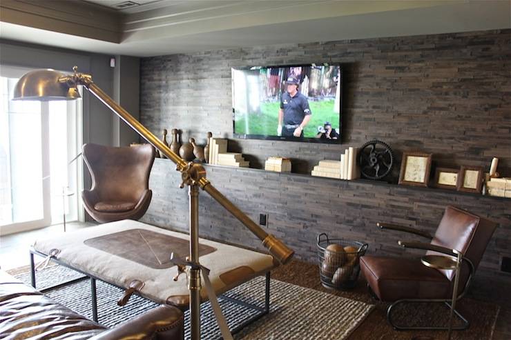 Parade of Homes - Media room with floor to ceiling stone accent wall accented with flatscreen TV and whatnots. Media room features Restoration Hardware 1950s Copenhagen Chair and brown leather chair paired with fabric covered coffee table over jute rug.