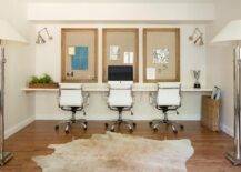 Homework room with a wall to wall desk features three task chairs, a framed pin board and sconces illuminating the space. A light brown cowhide rug layers over hardwood floors for a contemporary touch.