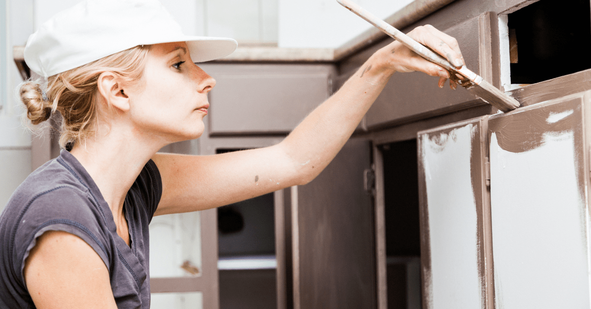 Closeup of woman holding paint brush and painting kitchen cabinets.