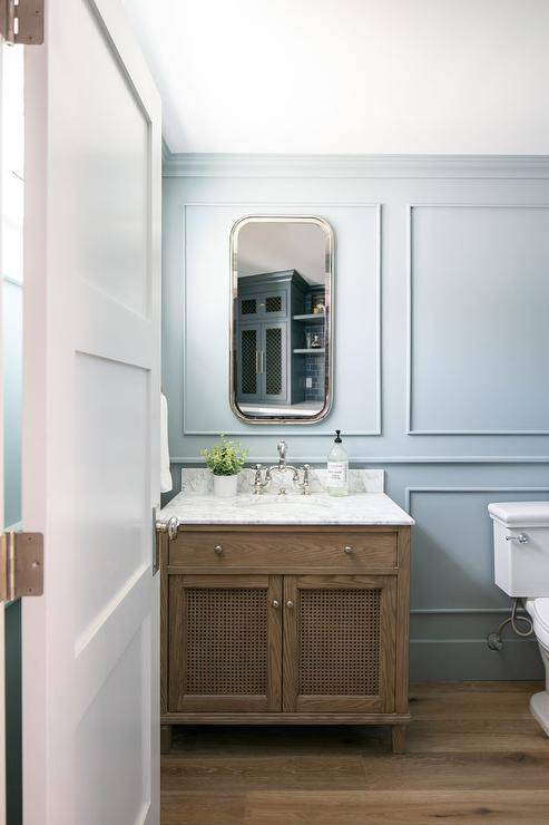 Brown washstand with a honed marble top fitted with a brown oak washstand fitted with a vintage deck mount faucet in a transitional bathroom. Floor to ceiling blue wainscoting adds a luxurious appeal to the overall design.