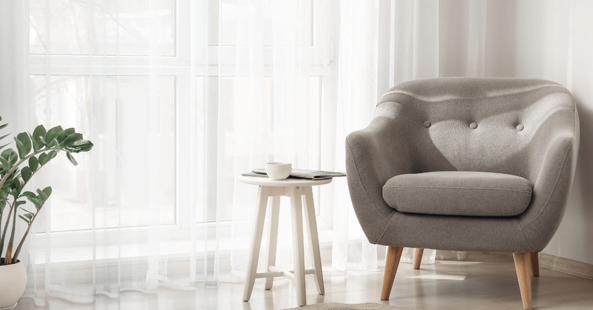 Living room with linen curtains and a grey single chair with wooden legs.