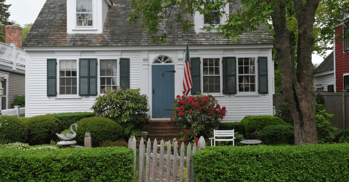 Older Cape Cod style house with American flag upfront.