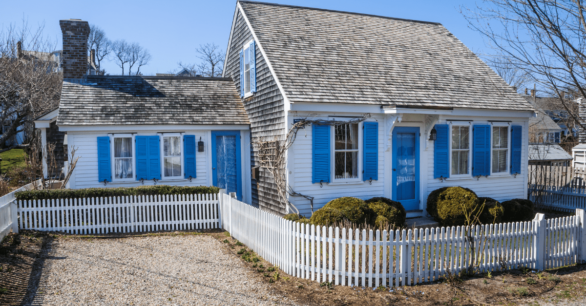 Older Cape Cod style house with white fencing.