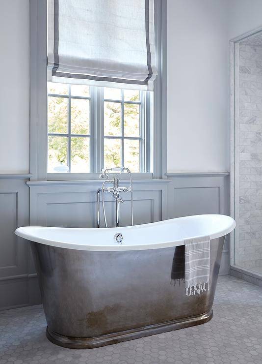 Master bathroom features a modern cast iron tub on marble hexagon floor tiles and gray wainscoting.