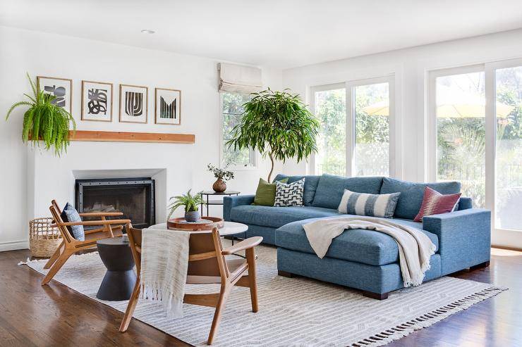 Blue sofa with a chaise lounge on a gray fringe rug in a transitional living room featuring mid-century modern accent chairs and a round marble top coffee table.