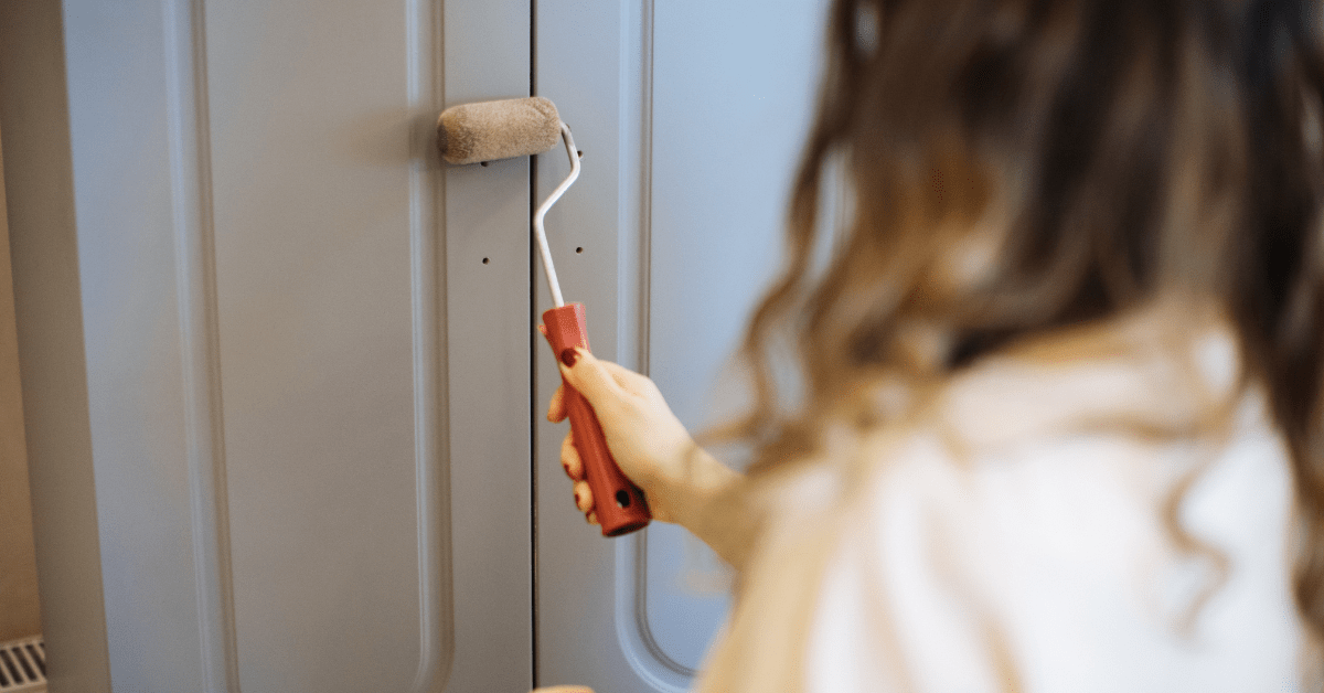 Person using a paint roller to apply paint to kitchen cabinets.