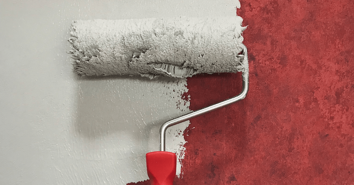 Paint roller painting over red textured wallpaper.