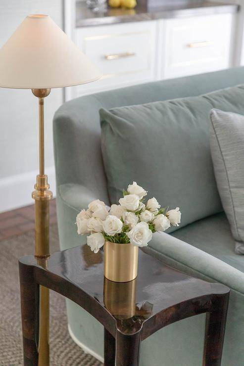 Living room features a sage green velvet sofa with a a brown lacquer end table illuminated by an antique brass floor lamp.