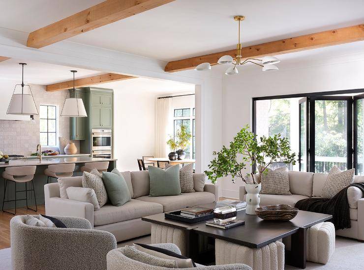 Livng room features a pebble gray couch accented with sage green pillows, a square wooden coffee table with cream boucle stools and gray boucle swivel chairs.