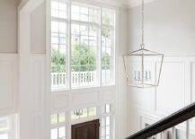 Two story foyer features wainscoting lit by a Darlana lantern.