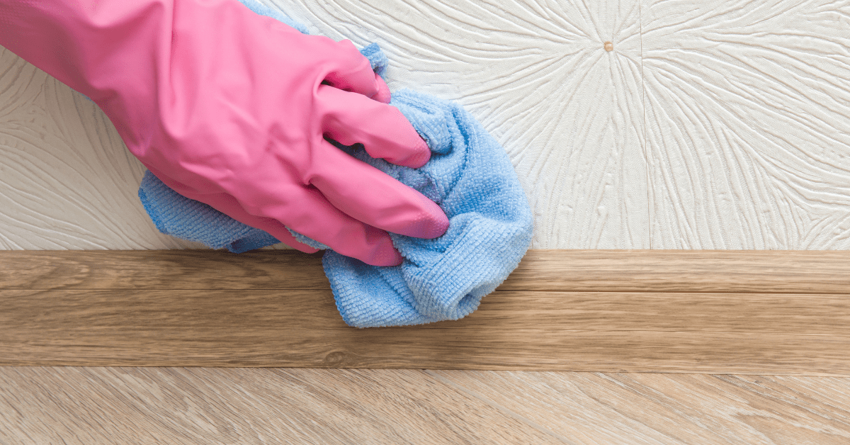 Hand in pink gloves using cloth to dry baseboards.