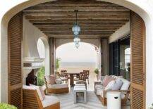 Rustic wood ceiling beams accent a furnished covered patio lit by blue glass Moroccan lanterns.