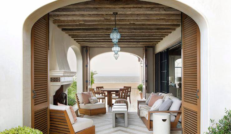 Rustic wood ceiling beams accent a furnished covered patio lit by blue glass Moroccan lanterns.