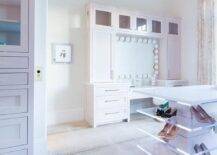 Contemporary custom closet features a white island fitted with lucite shoe shelves and placed on antelope carpeting. A pale pink makeup vanity boasts pink shaker drawers and cabinets fixed beneath glass front cabinets.