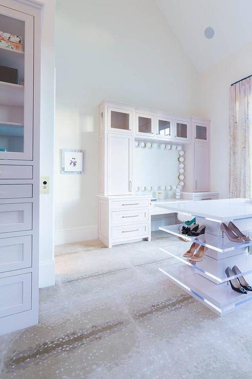 Contemporary custom closet features a white island fitted with lucite shoe shelves and placed on antelope carpeting. A pale pink makeup vanity boasts pink shaker drawers and cabinets fixed beneath glass front cabinets.