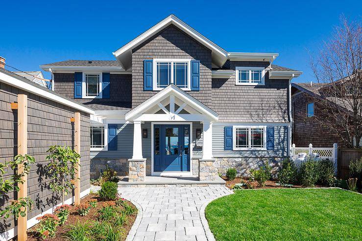 Craftsman style home features gray shingles, a blue front door, blue shutters and a stone paver walkway.