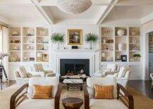 White built-in living room shelves fixed over white cabinets are accented with pale pink backs and flank a white fireplace mantel framing a black surround and styled under a gold framed portrait.