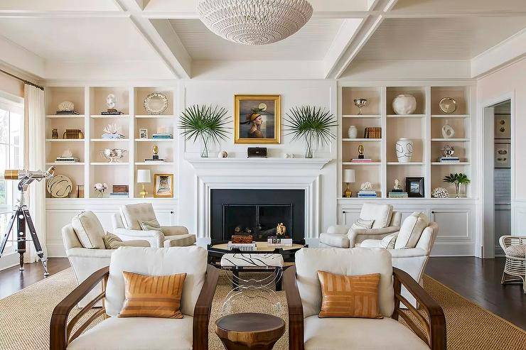 White built-in living room shelves fixed over white cabinets are accented with pale pink backs and flank a white fireplace mantel framing a black surround and styled under a gold framed portrait.