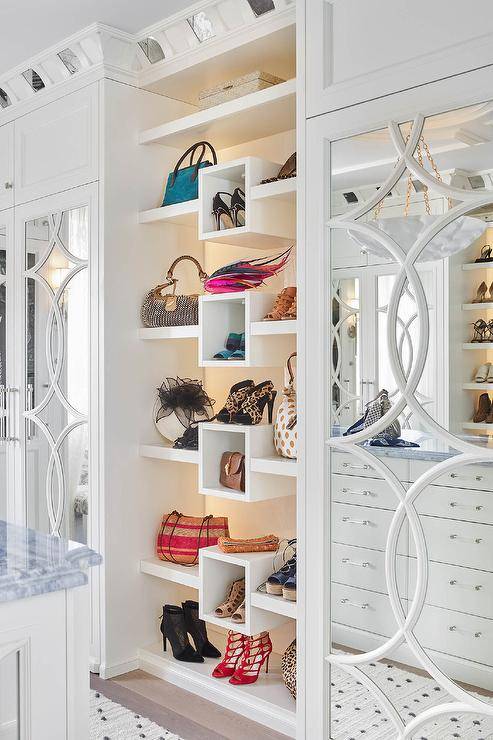 Glamorous white walk-in closet boasts custom bag and shoe shelves flanked by mirrored mullion wardrobe cabinets.