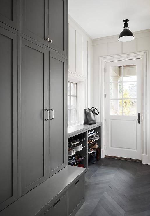 Charcoal gray chevron pattern floor tiles in a gray mudroom completed with gray built in cabinets and a gray bench. White plank walls contrast the gray hues in the mudroom bringing a perfectly balance of hues and interest. Stacked shoe shelves at the entry adds extra organizational appeal to the overall mudroom design.