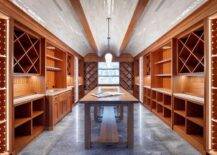 Spacious wine cellar features tiled barrel ceilings over built in shelves and a long wooden table atop a gray tiled floor.