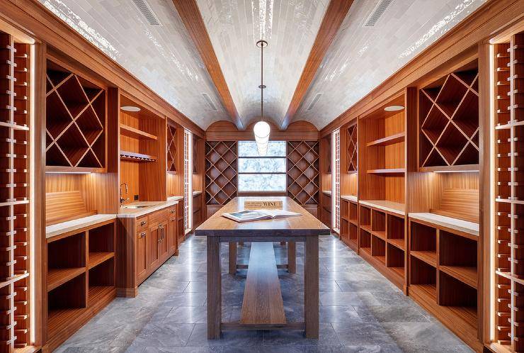 Spacious wine cellar features tiled barrel ceilings over built in shelves and a long wooden table atop a gray tiled floor.