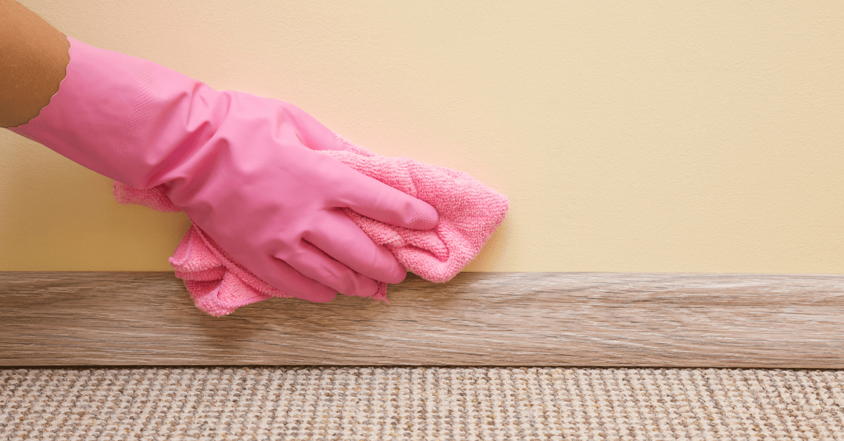 Hand in pink gloves cleaning baseboards and walls.