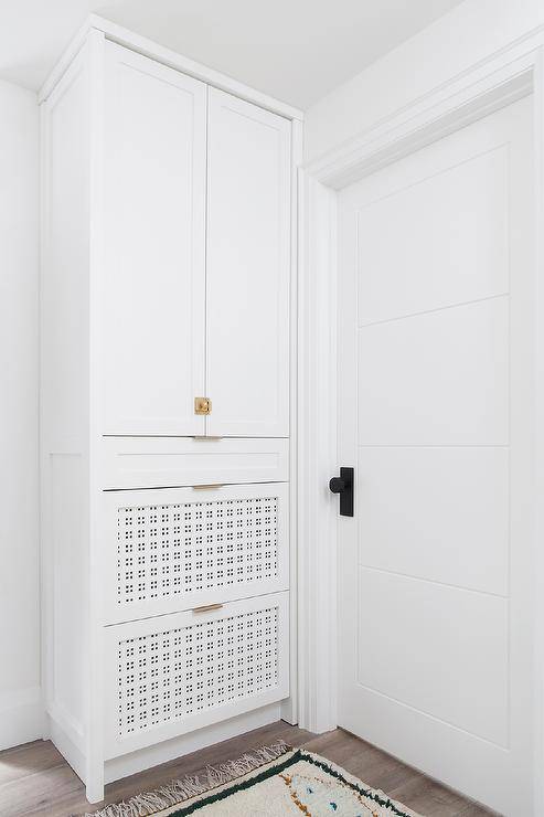Entry built-in cabinets with pierced shoe drawers finished with antique brass vintage latch hardware on gray wash wood floors.