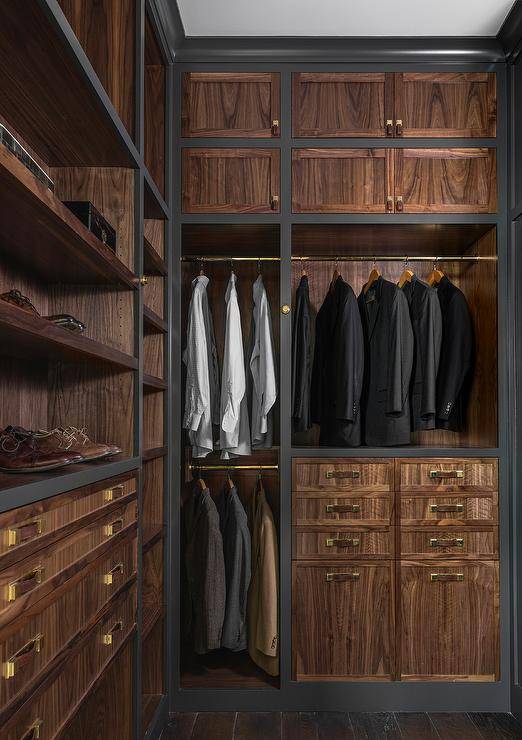 Men's closet design features veneer cabinet doors adorned with leather and brass hardware, built in shoe shelves and brass clothes rails.