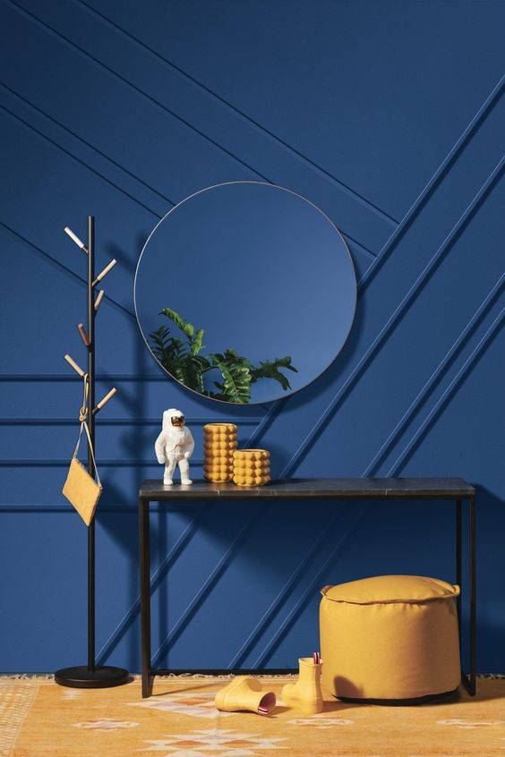 indigo blue accent wall with round mirror, light brown stool and narrow table