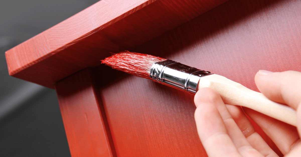 Small brush painting a piece of furniture red.