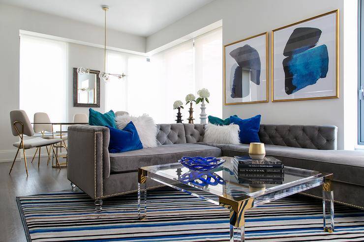 A modern and glamorous living room and Manhattan with a gray tufted sectional, lucite cocktail table, bold artwork and a cowhide striped area rug. Photo by Raquel Langworthy