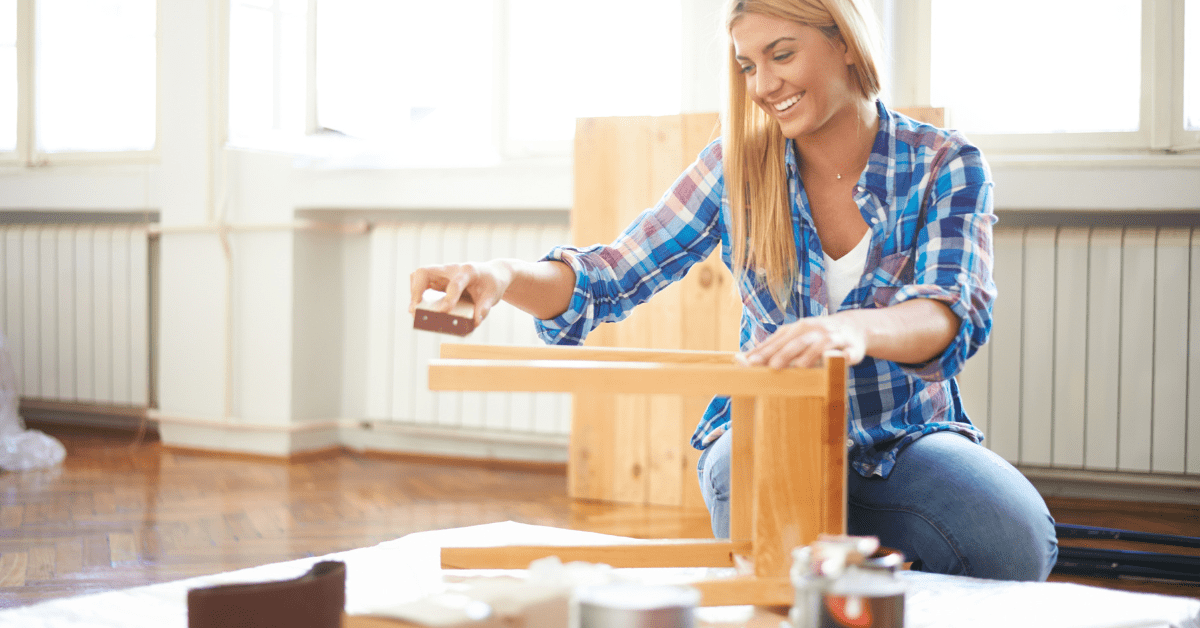 Woman sanding a wooden piece of furniture to prepare it for paint.