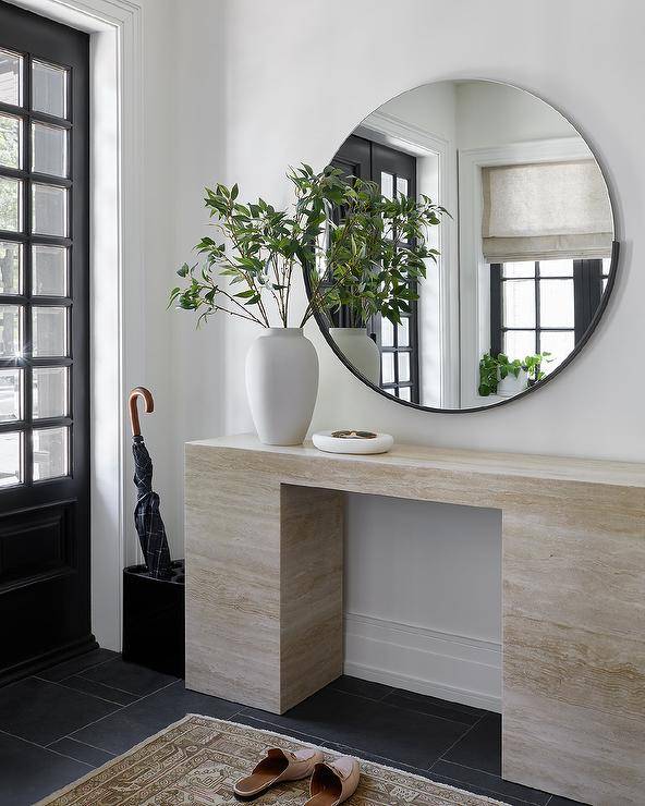 A large round black mirror hangs in an entry over a marble console table.