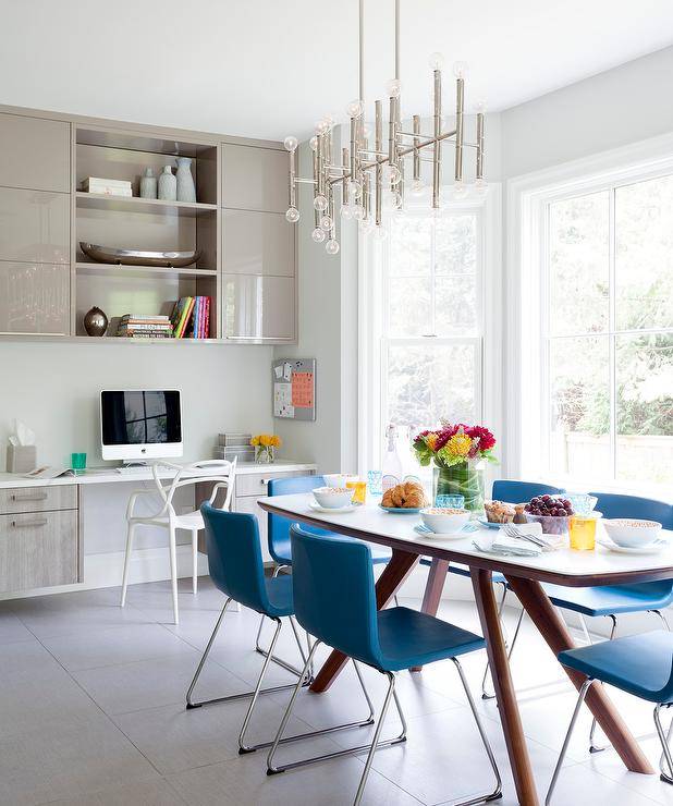 Masters Chair at a built-in taupe floating desk in a kitchen space furnished with a mid-country modern dining table and blue dining chairs. A silver bamboo chandelier adorns the dining set with a contemporary appeal.
