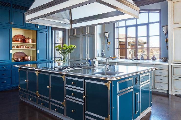 Spacious kitchen features a peacock blue metal island with stainless steel countertop and dual gas cooktops and blue cabinets.