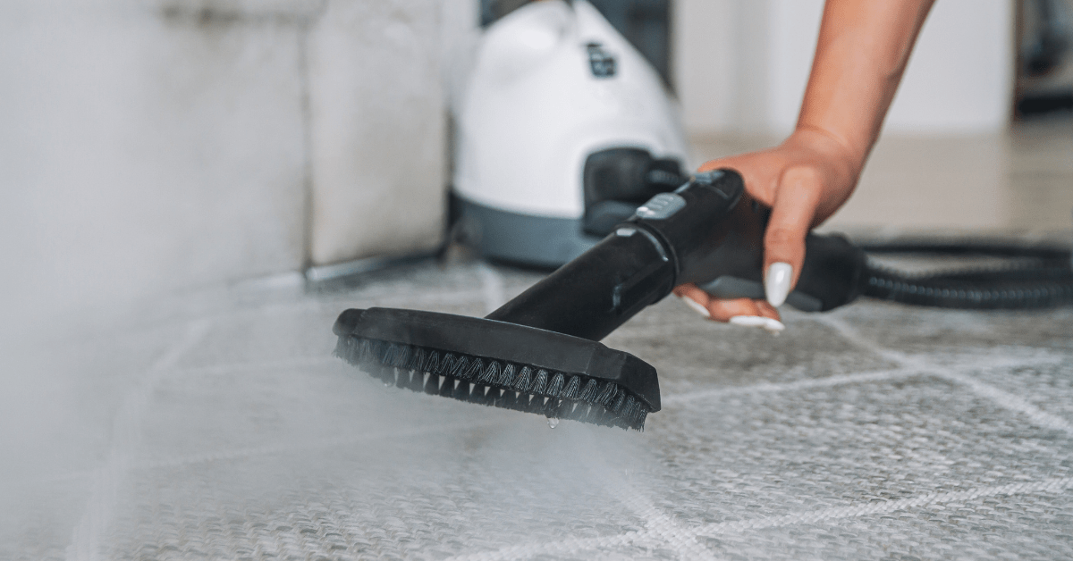 A closeup of someone's hand using a steam cleaner on carpet.