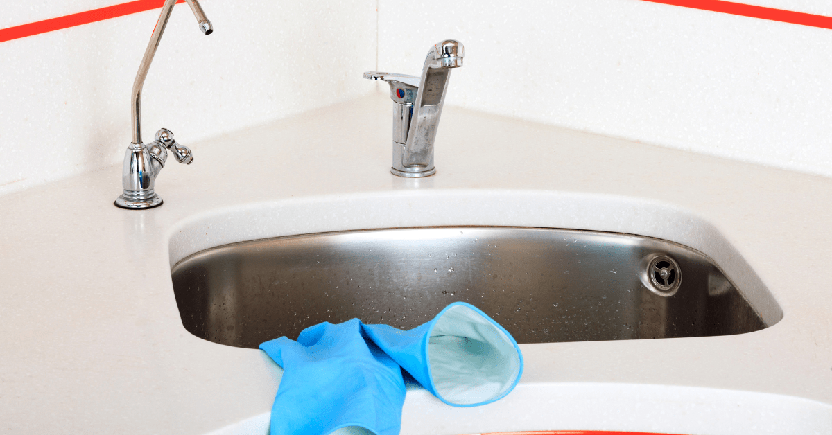 A pair of blue gloves drying on a clean stainless steel sink.
