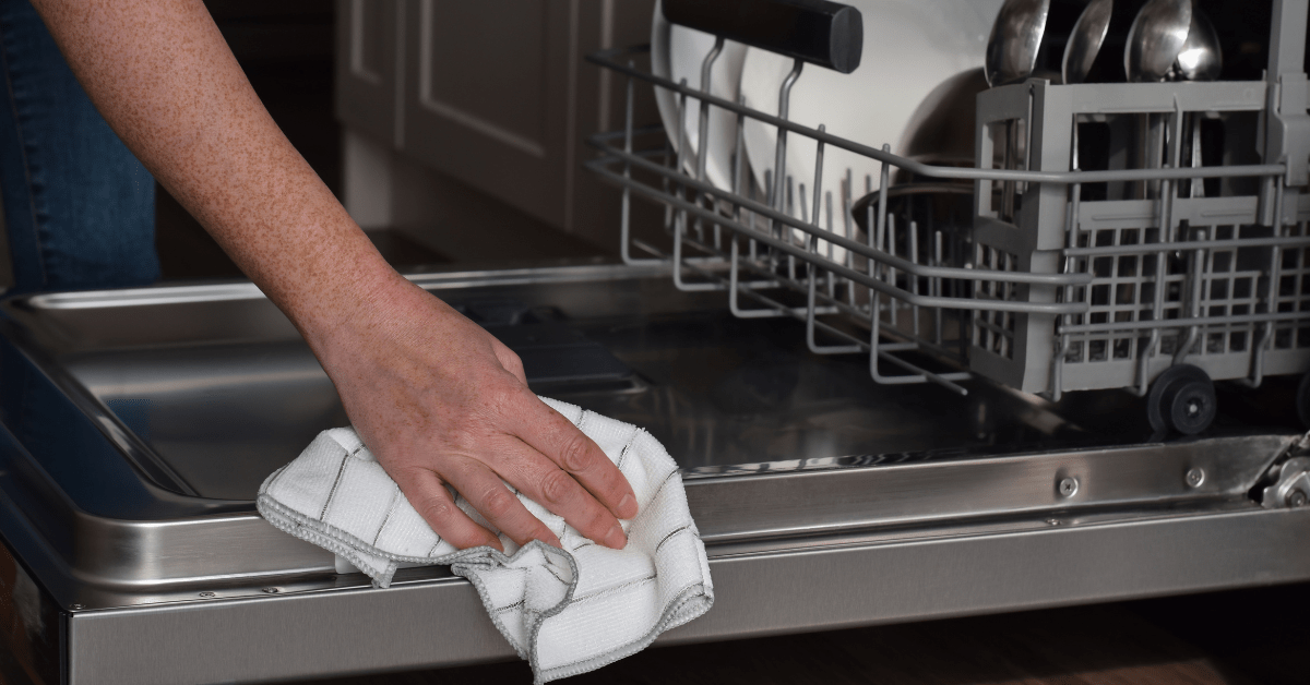 Wiping down a dishwasher with a cloth.