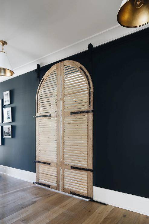 Black mudroom walls contrast stunning arched louvered doors on rails.