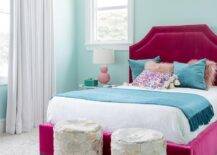 Blue velvet pillows decorate a fuchsia velvet tufted bed in a girls bedroom designed with pink double gourd lamps on nightstands. An aqua blue wall contrast the bold fuchsia headboard with the perfect balance while gray and gold hexagon stools accent the foot of the bed.