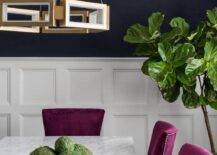 Fuchsia dining chairs and a marble and brass dining table takes notice with its classic materials and stunning bold colors. Navy blue walls combined with white wainscoting trim bring this dining room to life with accents like a fiddle leaf fog plant and a brass gemeotric pendant.
