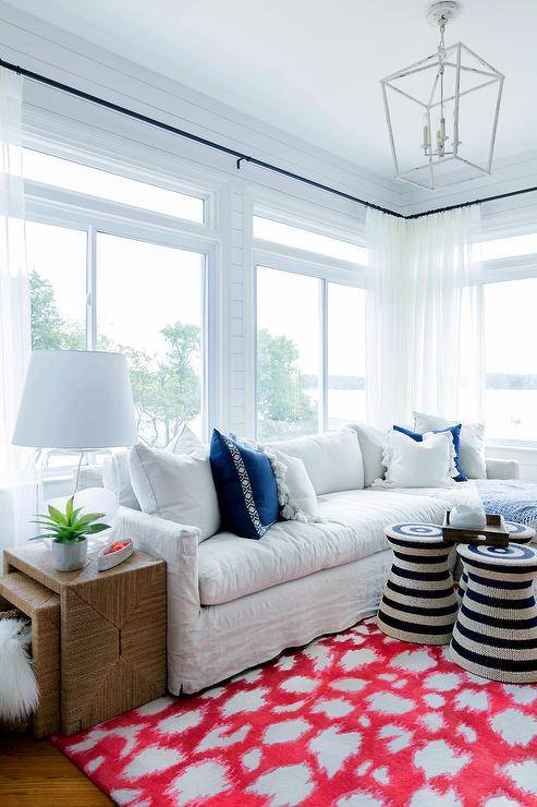 Red animal print rug in a living room with a white slipcovered sectional accented with blue and white pillows. Black stripe woven accent tables bring the finishing touch to the living space with a contrast to the bold area rug.